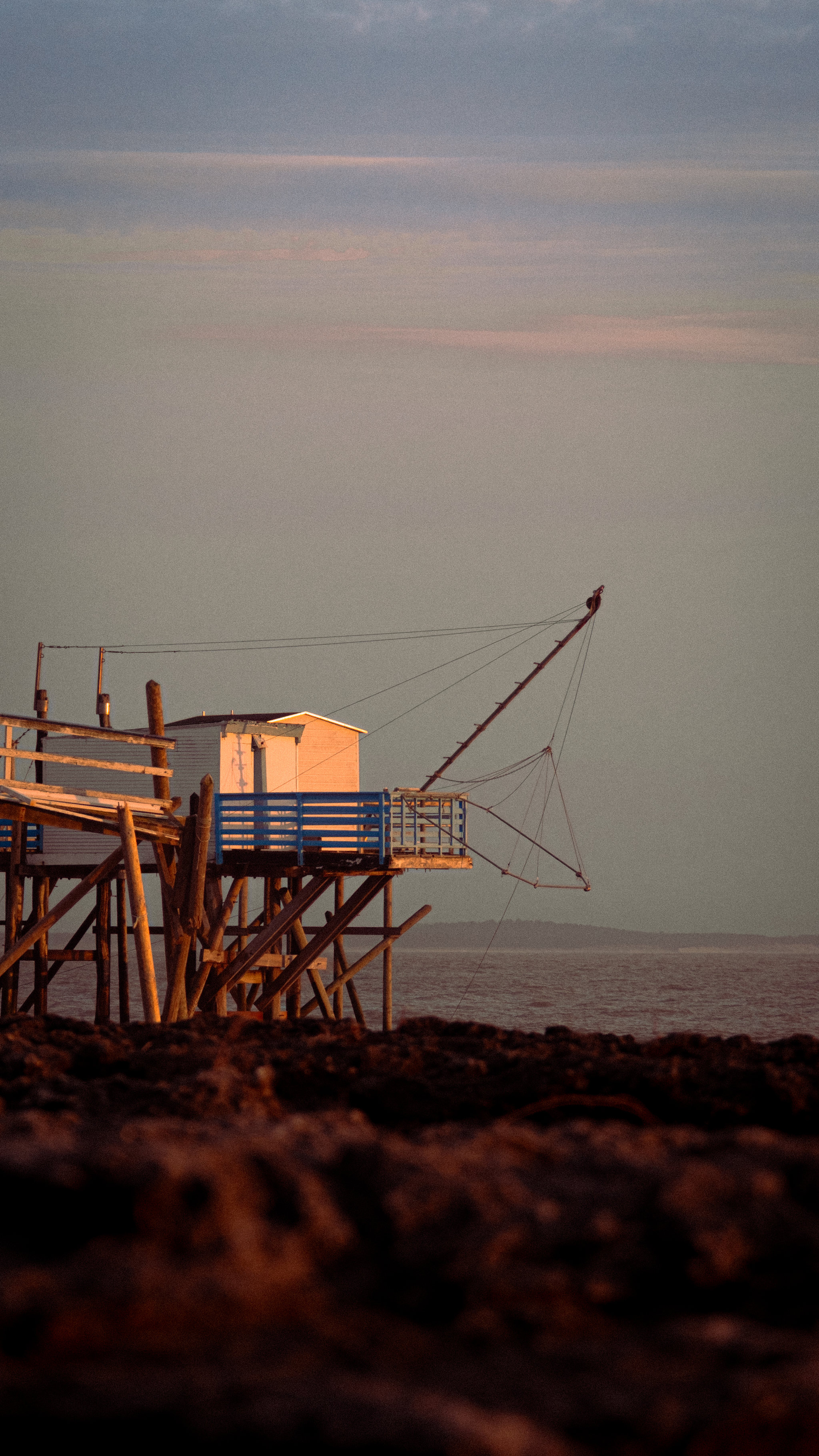 A fishing structure extending above a low coastal horizon at dusk.