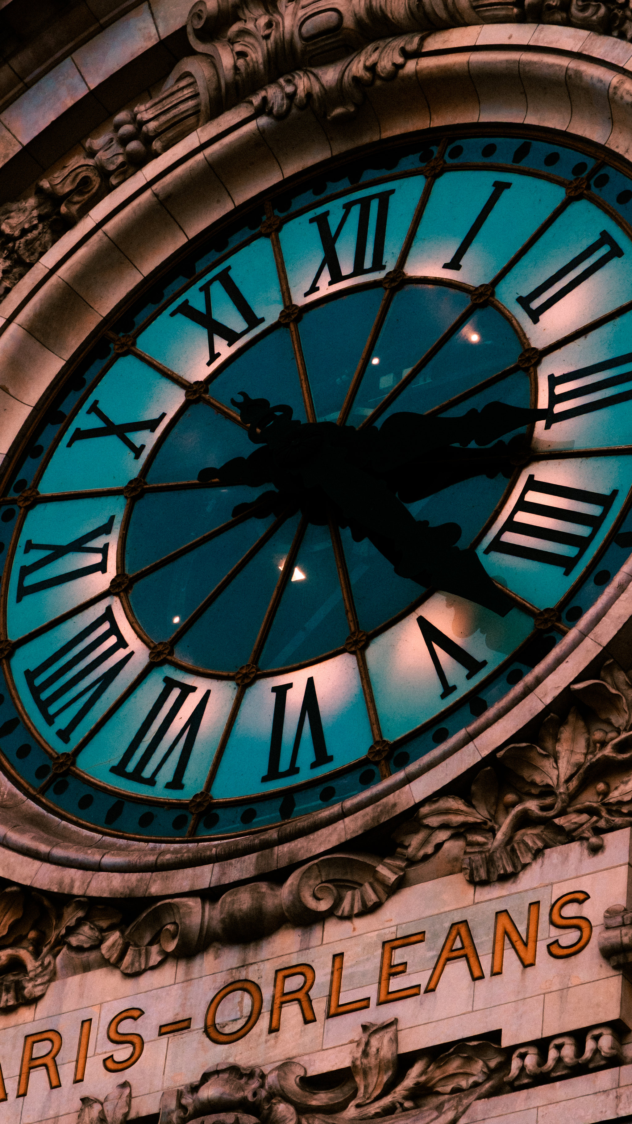 A turquoise railway clock framed by carved stone architecture.