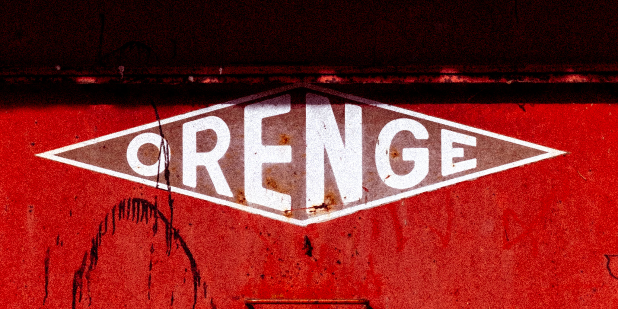 A red illuminated sign bearing the word orange on a textured wall.