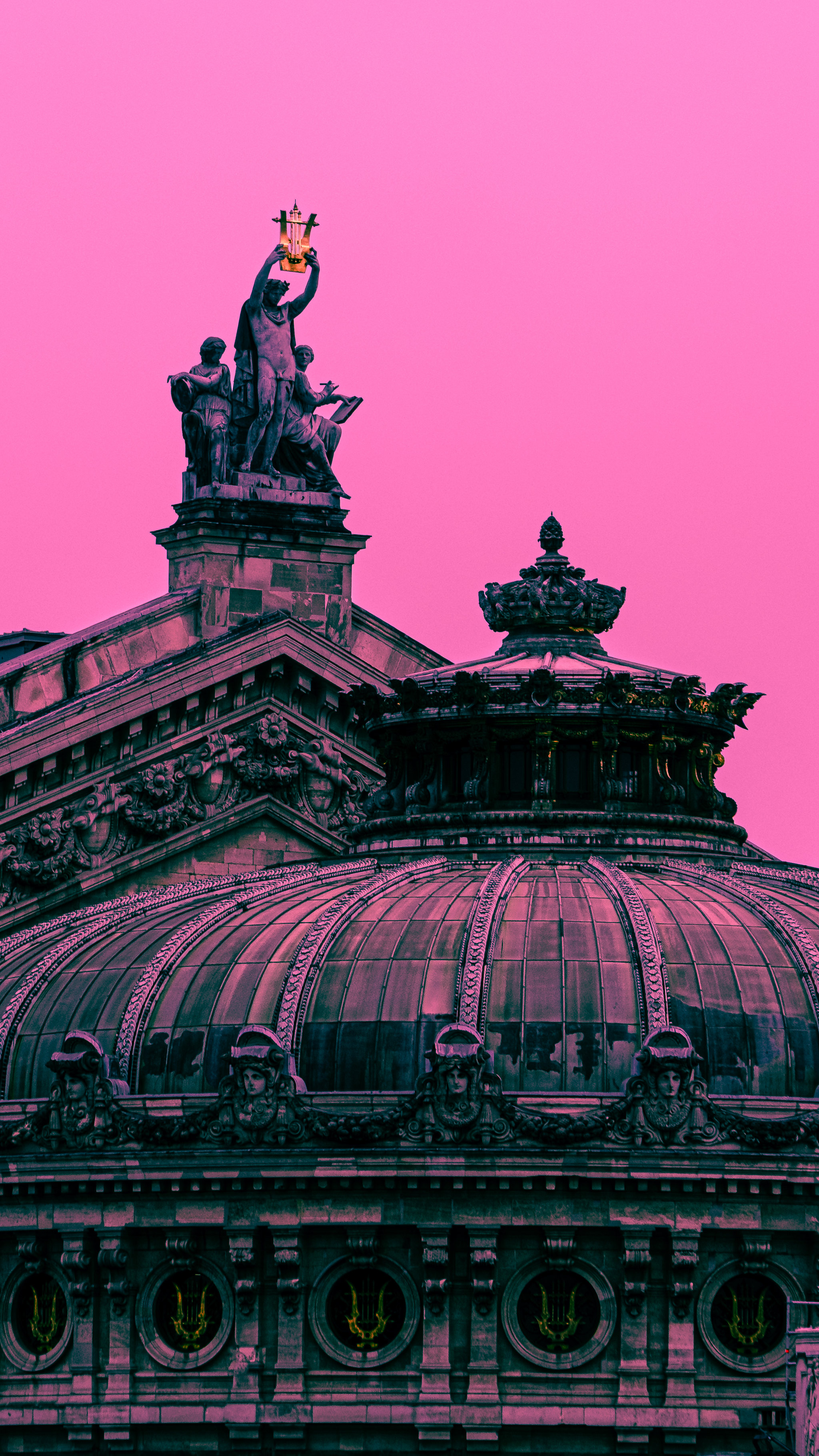 An ornate domed building and rooftop statue beneath a pink sky.