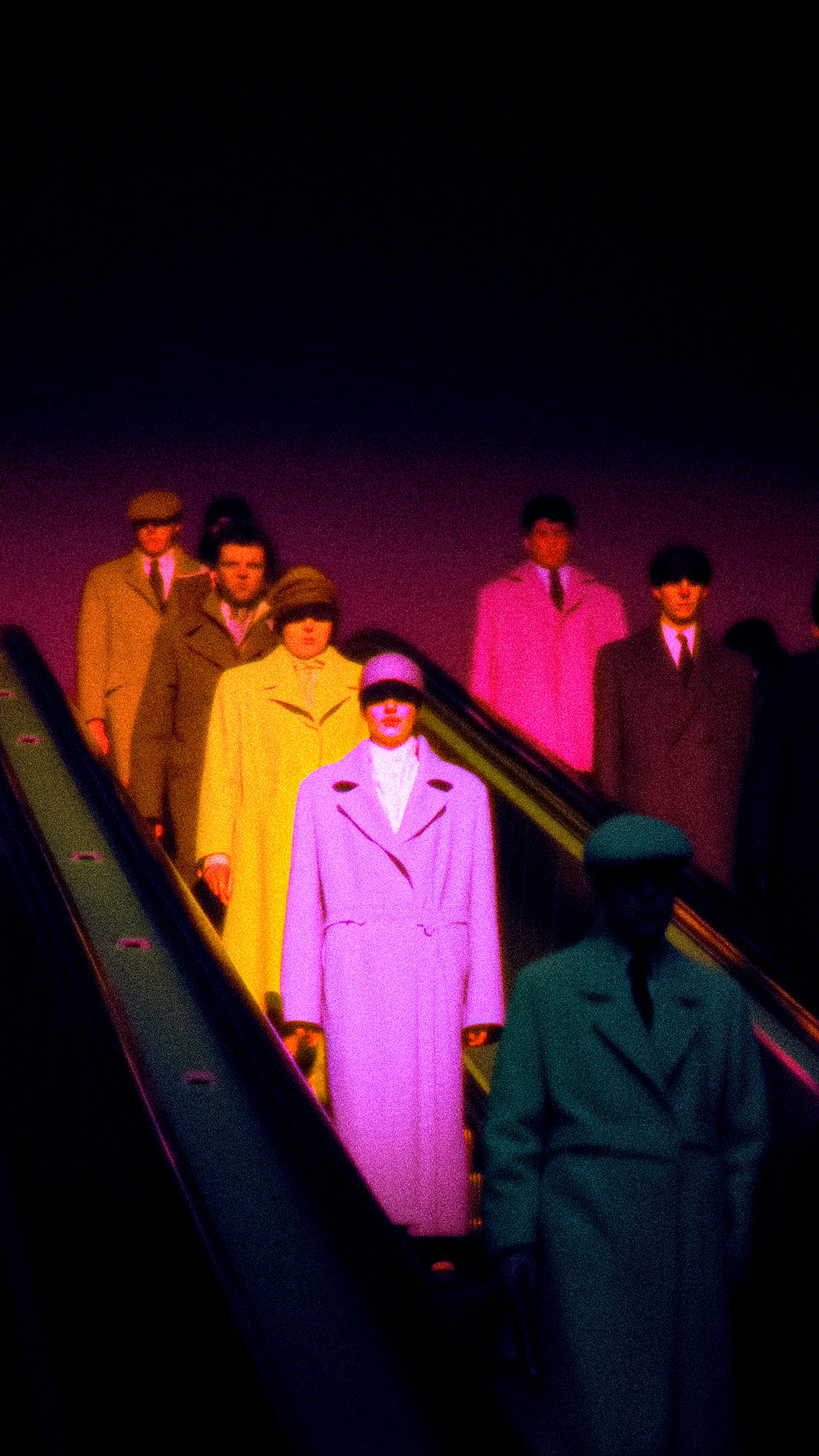 Figures in brightly coloured coats descending a dark escalator.