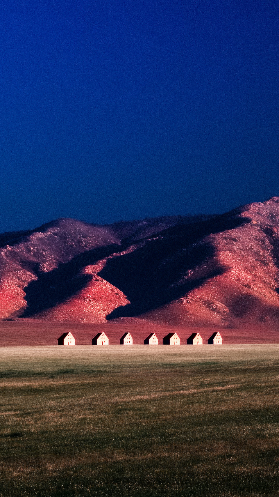 Five white houses aligned before a pink mountain beneath a deep blue sky.