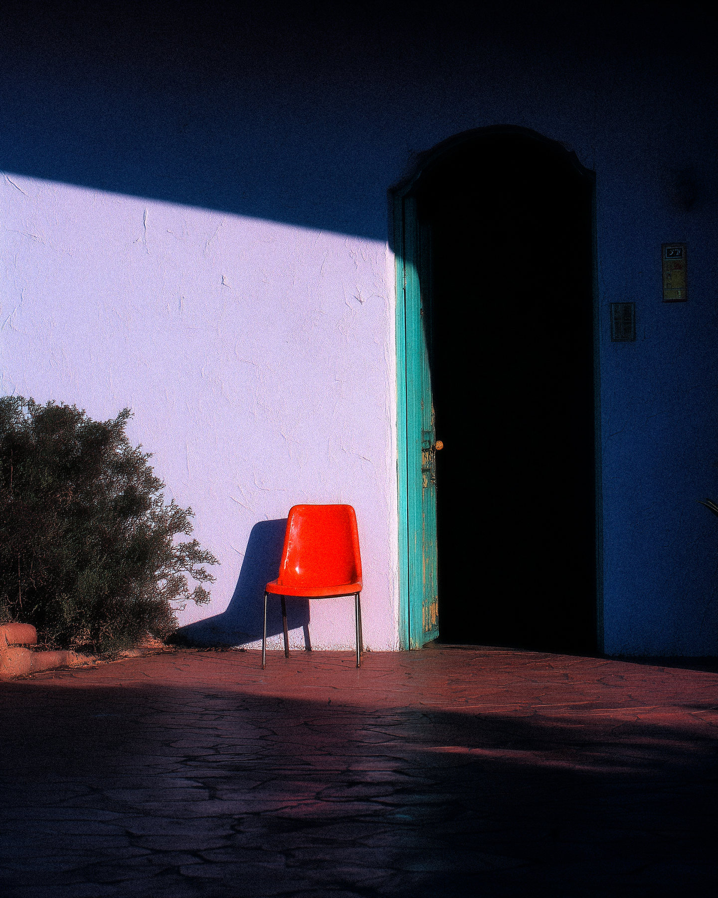 A red chair outside a white building with a dark open doorway.