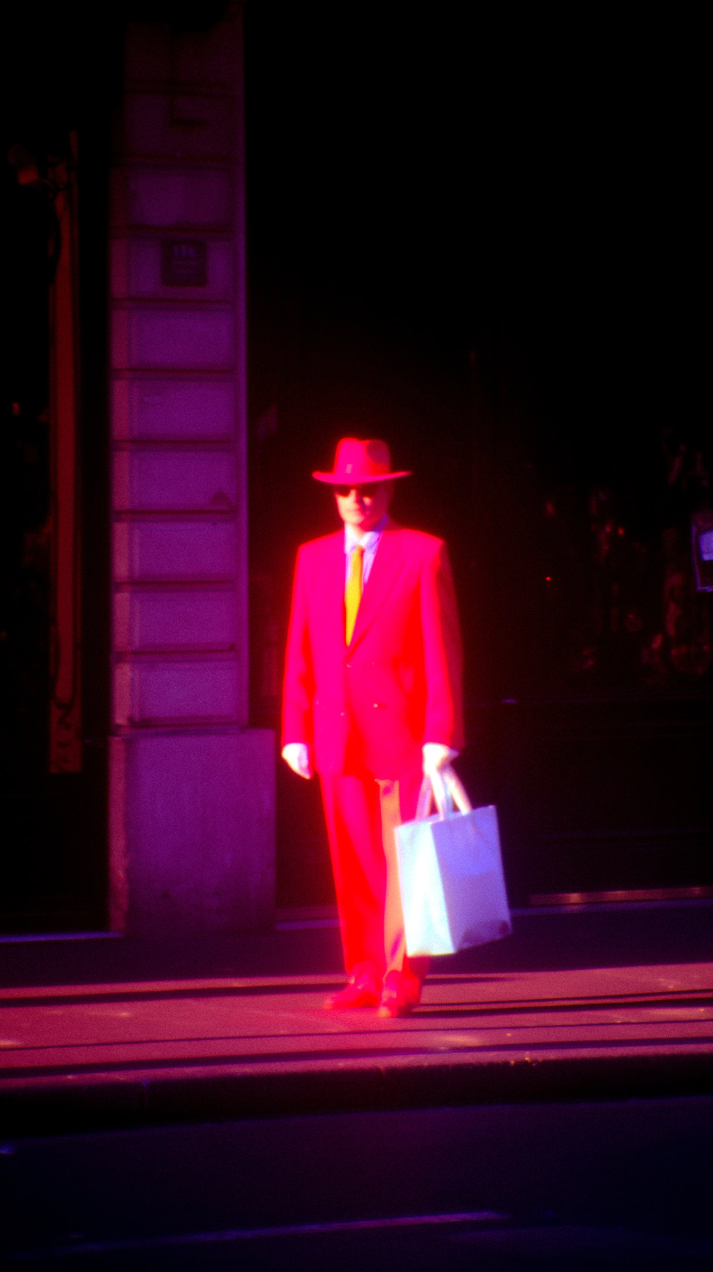 A solitary figure in a red suit and hat carrying a white bag at night.