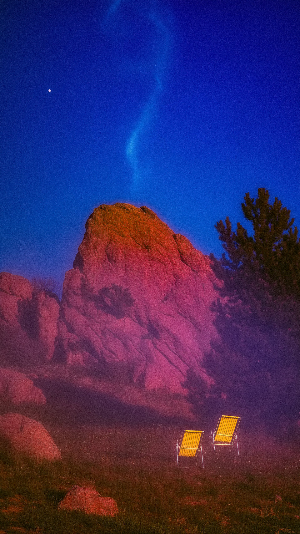 Two yellow chairs facing a pink rock formation under a blue sky.