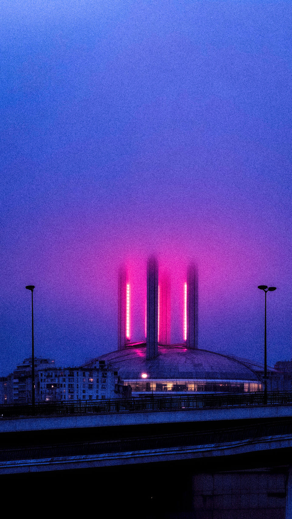 Three vertical magenta light columns rising beside a futuristic city.
