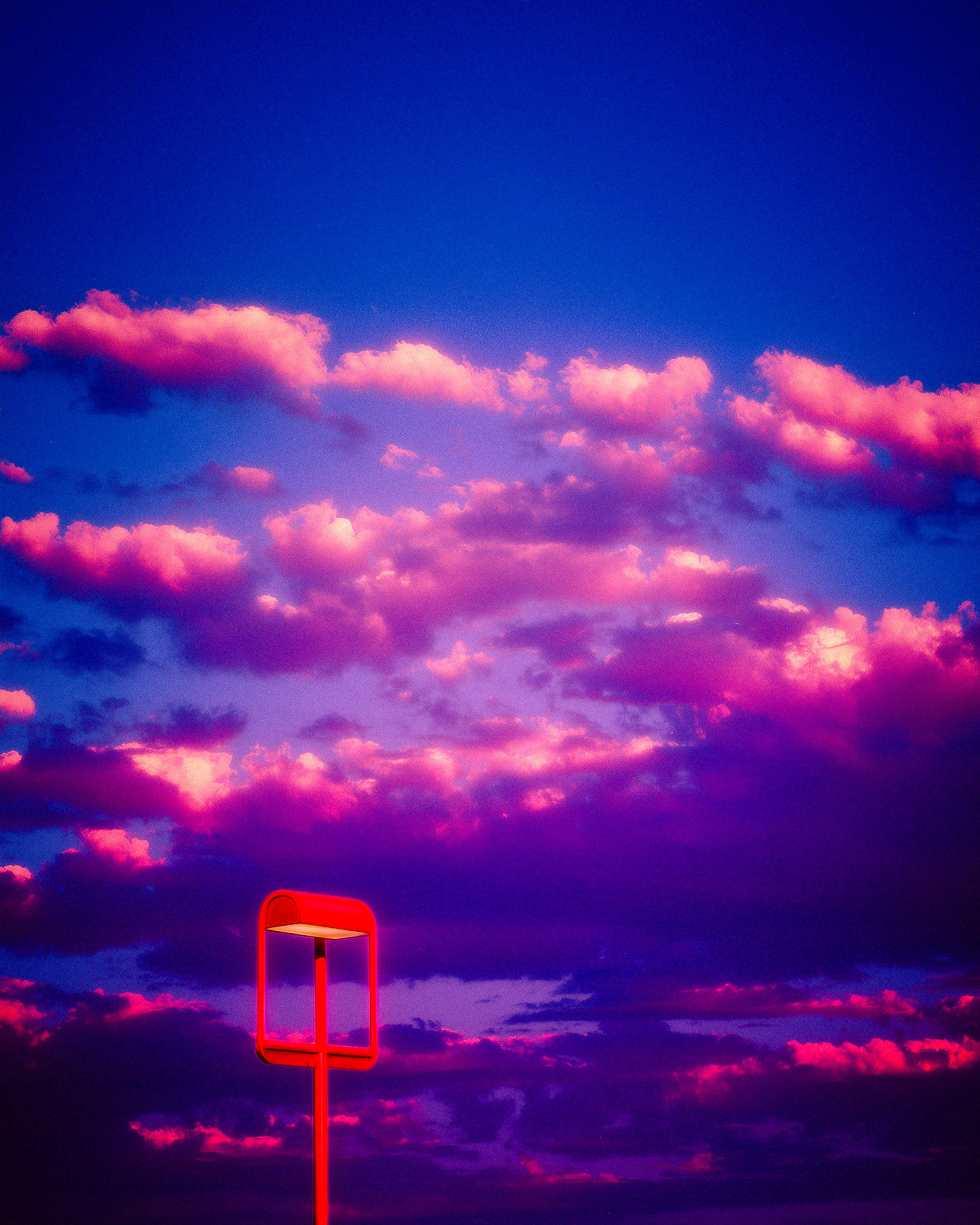 A small orange beacon below luminous pink clouds in a deep blue sky.