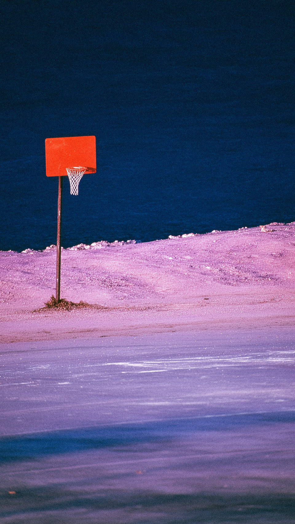 An orange square sign standing beside dark blue water and a pale shore.