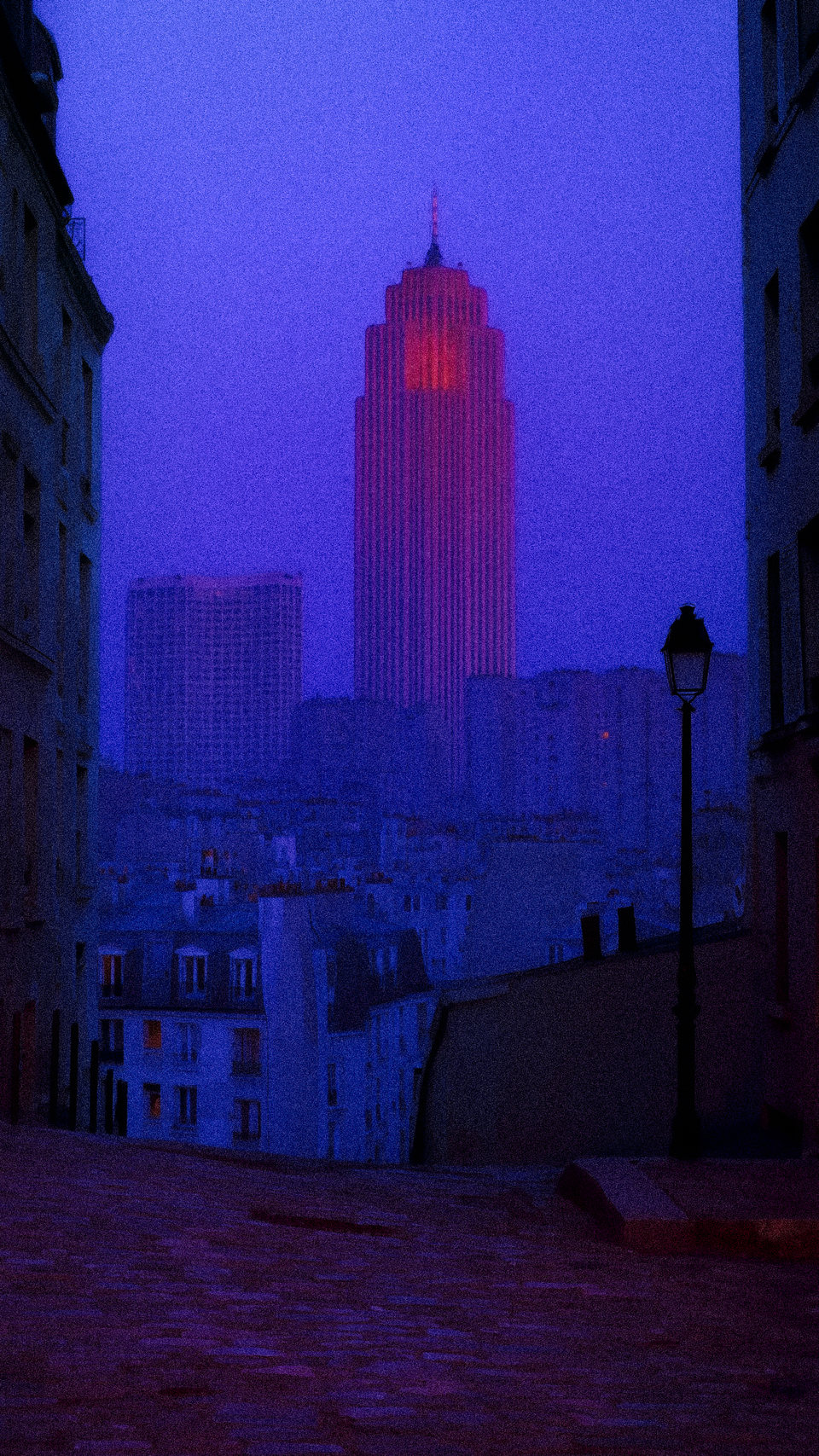 A tall distant tower seen between dark buildings in purple twilight.